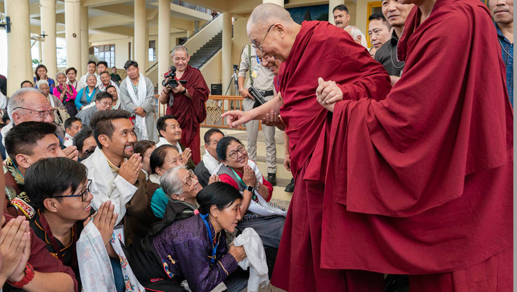 Sa Sainteté le Dalaï-Lama salue les membres de l'auditoire alors qu'il se dirige vers sa résidence à la fin de sa rencontre avec les participants à la conférence internationale sur l'approche de la voie du milieu dans la cour du temple tibétain à Dharamsala, Inde, le 30 mai 2018. Photo de Tenzin Choejor